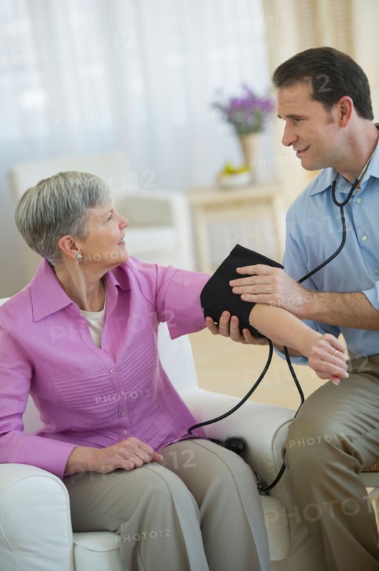 Smiling man taking senior woman's blood pressure.