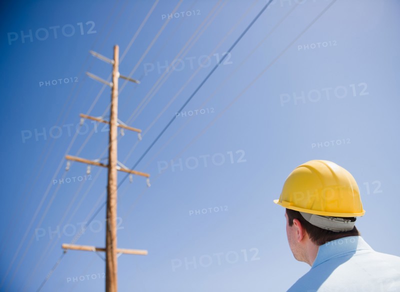 Man in hard hat looking at telephone pole. Photo : Jamie Grill Photography