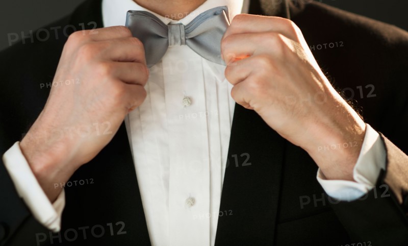 Studio shot of bridegroom adjusting bow tie.