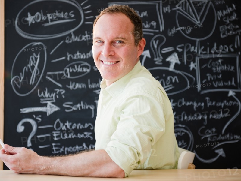 Businessman sitting at table against blackboard. Photo: Jamie Grill