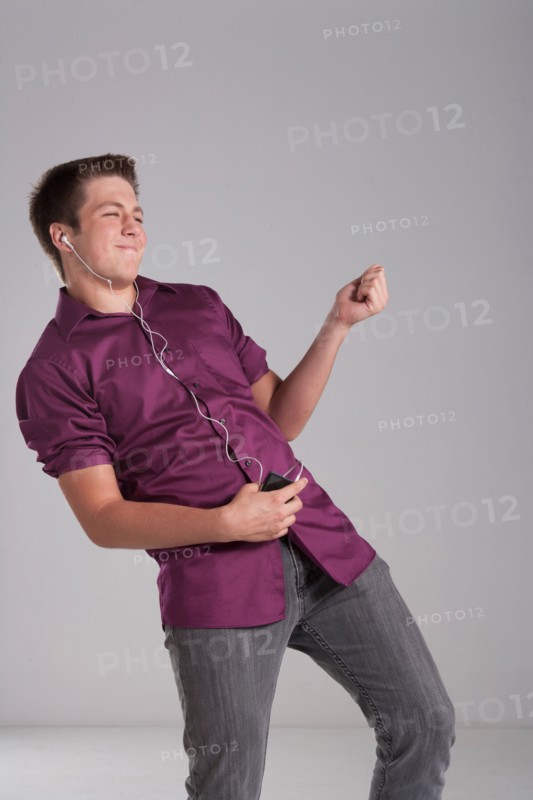 Portrait of smiling teenager playing air guitar, studio shot. Photo : Rob Lewine