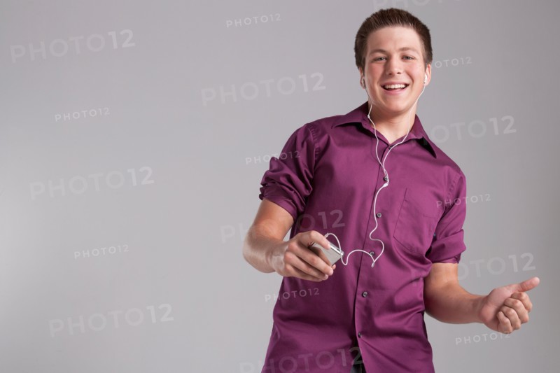 Portrait of smiling teenager listening mp3 player, studio shot. Photo: Rob Lewine