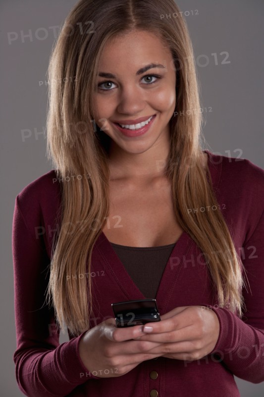Portrait of teenage girl (16-17) with mobile phone, studio shot. Photo : Rob Lewine