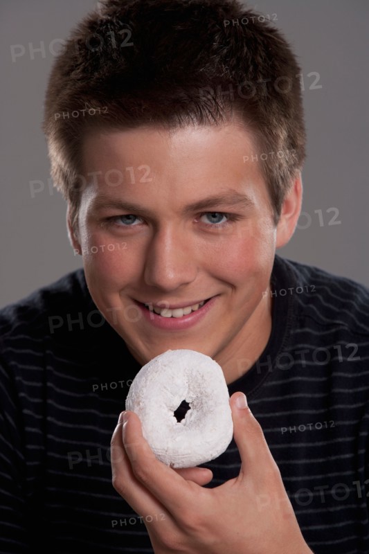 Portrait of teenage boy (16-17) with donut, studio shot. Photo : Rob Lewine