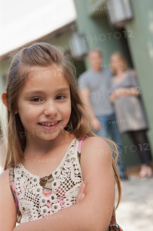 Portrait of cheerful girl (6-7) with parents in background. Photo: Rob Lewine