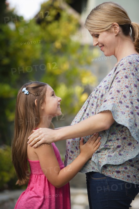 Pregnant mother standing face to face with daughter (6-7) . Photo : Rob Lewine