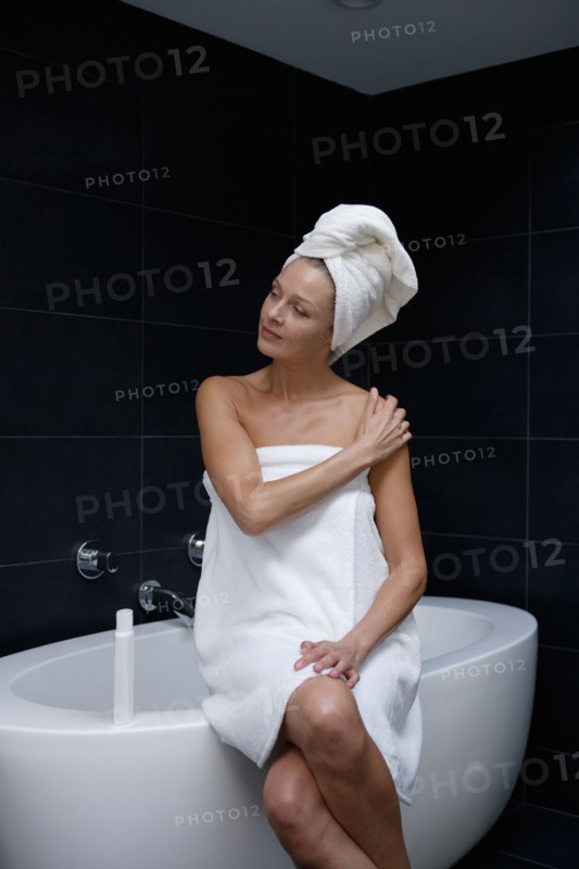 Mature woman sitting in bathroom wrapped in towel. Photo : Rob Lewine