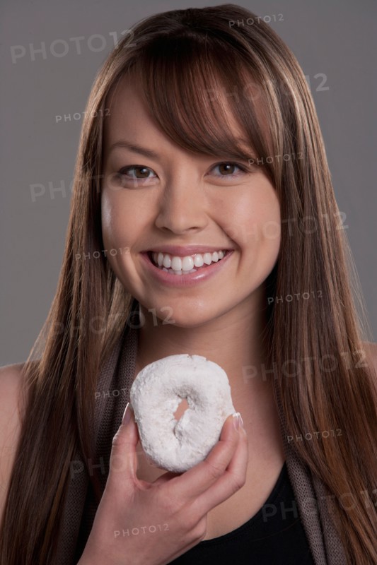 Portrait of young woman with donut, studio shot. Photo : Rob Lewine