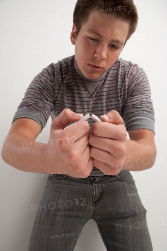 Teenage boy (16-17) breaking cigarette, studio shot. Photo: Rob Lewine