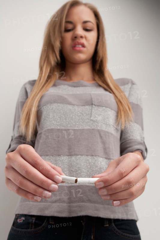 Teenage girl (16-17) breaking cigarette, studio shot. Photo: Rob Lewine