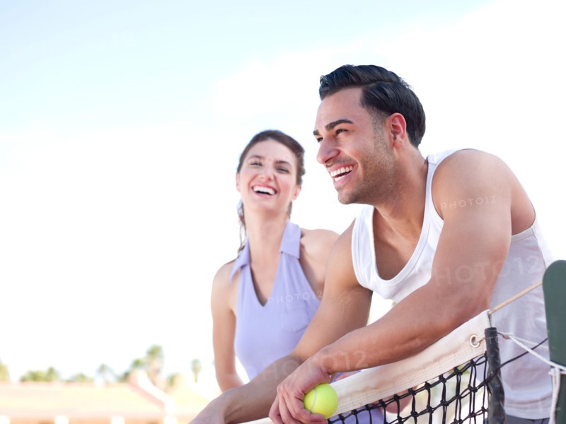 Smiling couple standing near tennis net. Photo : db2stock