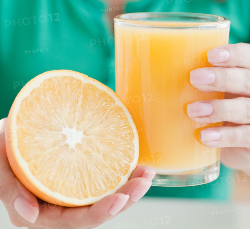 Close up of woman's hands holding half of orange and glass of juice. Photo : Jamie Grill