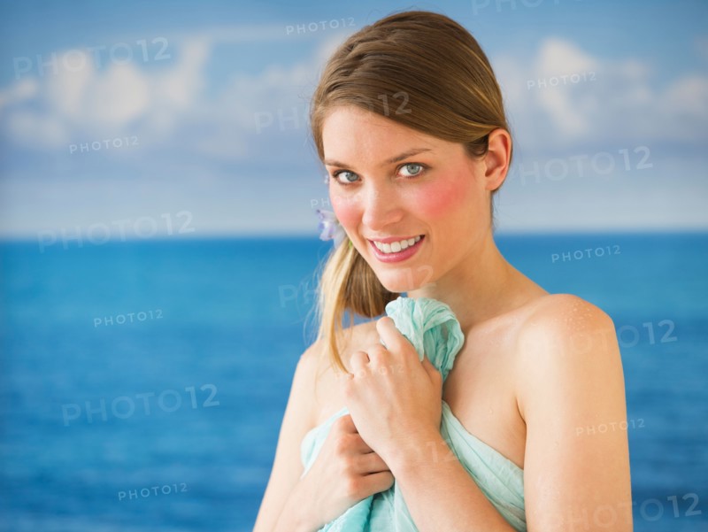 Portrait of young woman holding towel by sea.