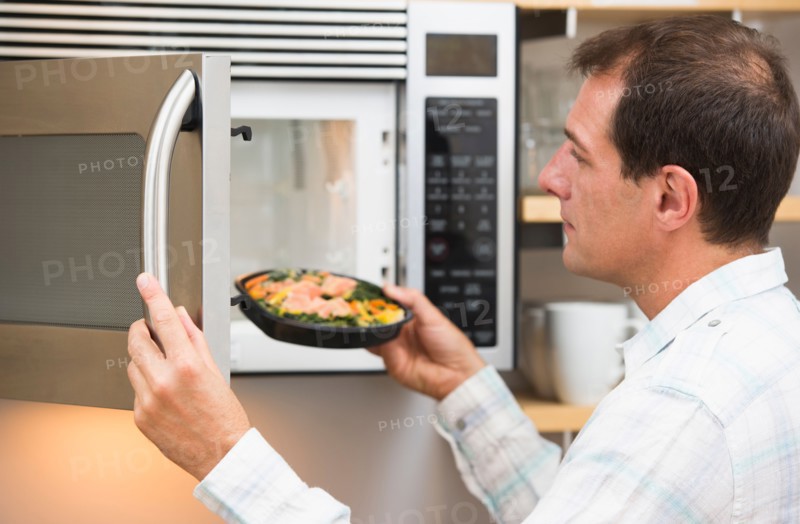 Man inserting meal in microwave oven.