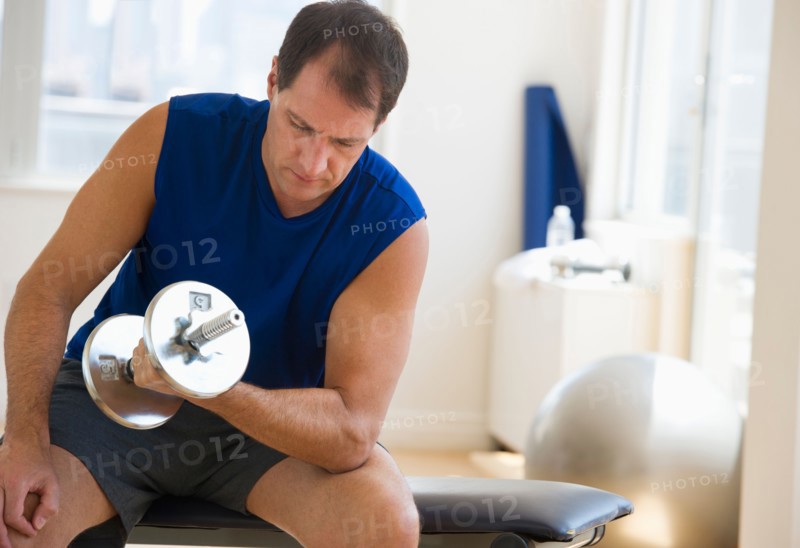 Mature man lifting weights in gym.