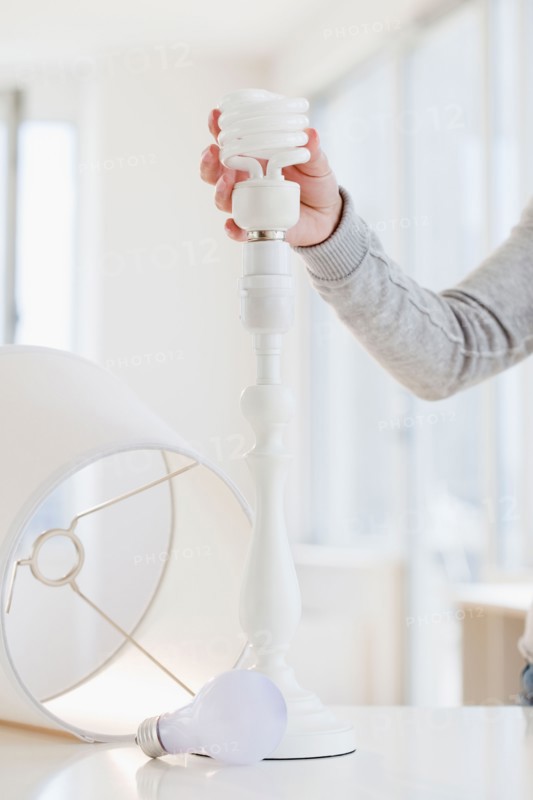 Woman changing classic bulb to energy efficient bulb. Photo : Jamie Grill