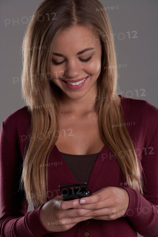 Portrait of teenage girl (16-17) with mobile phone, studio shot. Photo : Rob Lewine