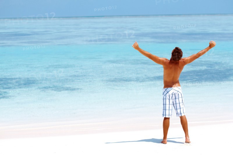 Man standing with his arms wide open on beach. Photo : momentimages