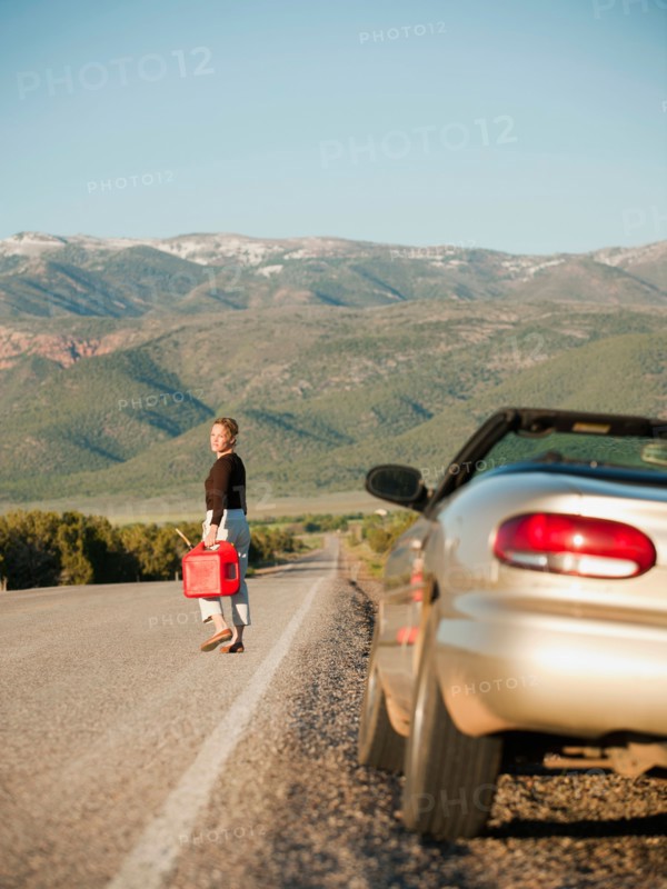 USA, Utah, Kanosh, Woman carrying canister walking along empty road, her car parked on roadside. Photo: Erik Isakson
