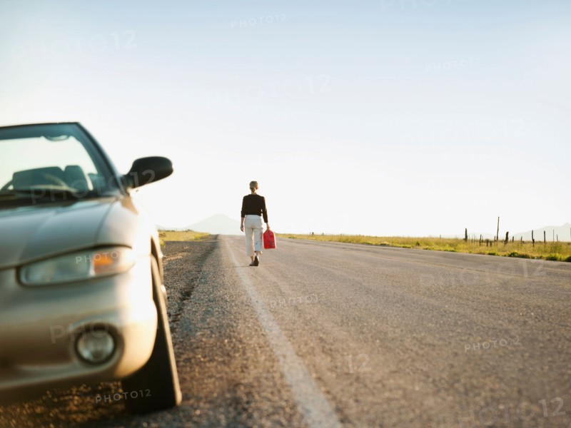 Woman carrying canister walking along empty road, her car parked on roadside. Photo: Erik Isakson