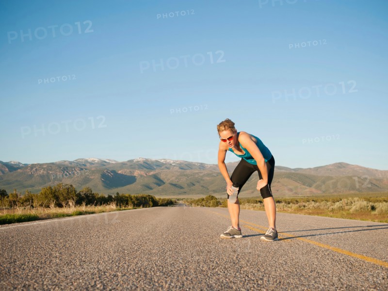 USA, Utah, Kanosh, Mid adult woman taking break from running on empty road.