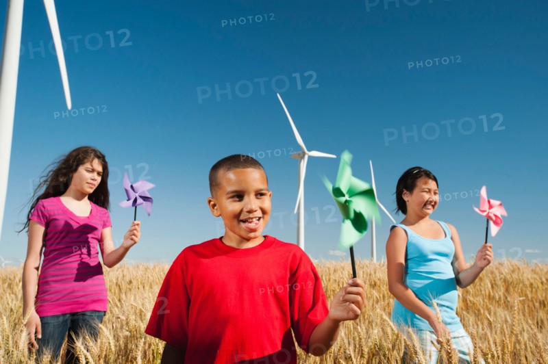 USA, Oregon, Wasco, Pre-teen girls (10-11) and boy (8-9) holding fans in wheat field in front of wind turbines.
