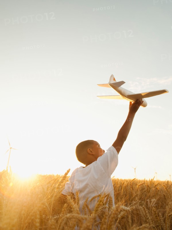 Boy (10-11) playing with toy aeroplane in wheat field.