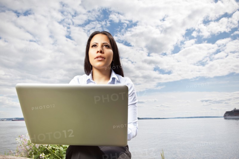 Young businesswoman using laptop on lakeshore. Photo : Take A Pix Media