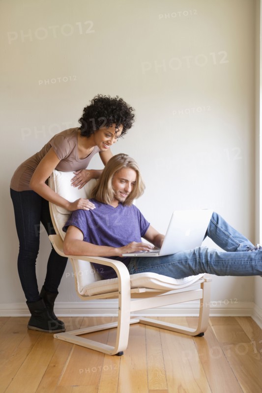 Young woman looking at man using laptop at home. Photo : Rob Lewine