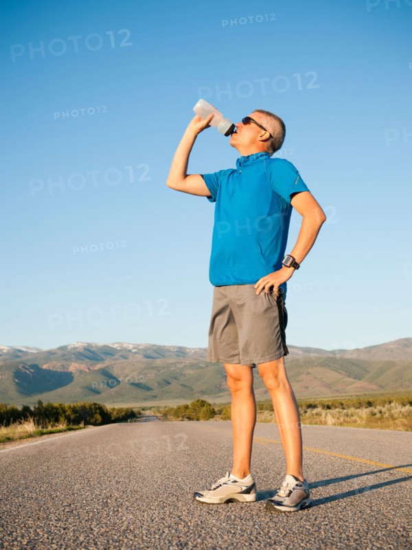 Mid adult an drinking water while taking break from running on empty road.