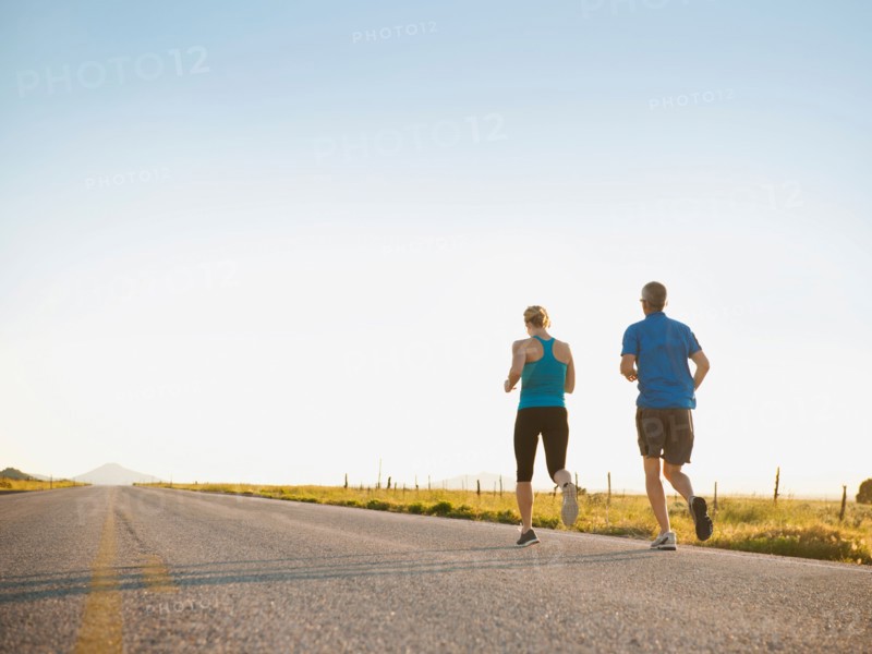 Mid adult couple running on empty road. Photo: Erik Isakson