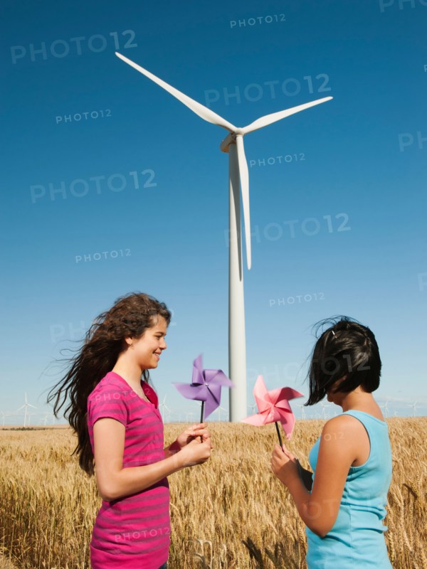 USA, Oregon, Wasco, Girl (10-11, 12-13) holding fans in wheat field in front of wind turbines.