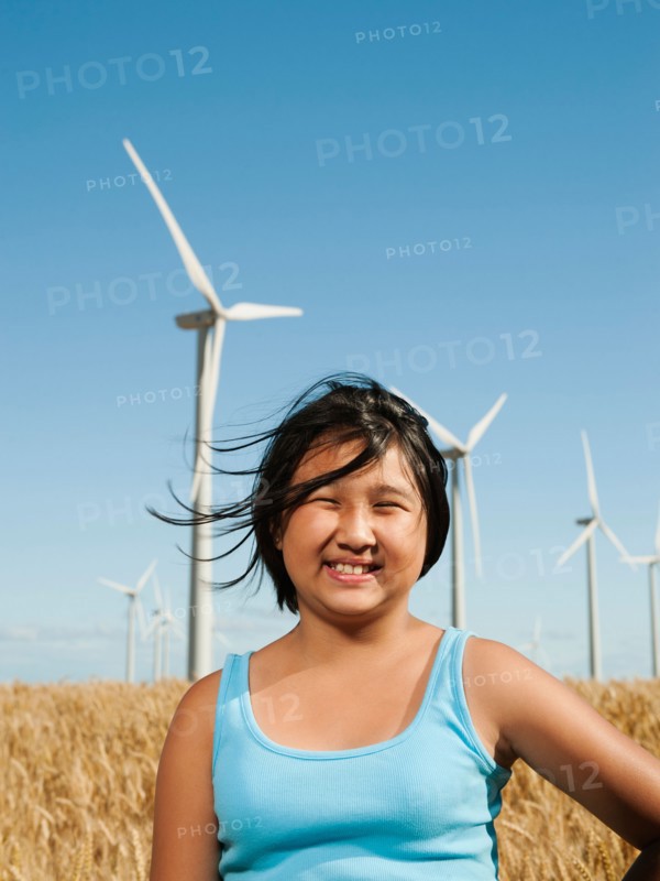 USA, Oregon, Wasco, Cheerful girl (10-11) standing in wheat field with wind turbines in background.