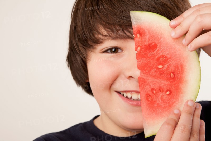 Studio portrait of boy (10-11) holding slice of watermelon. Photo : Rob Lewine