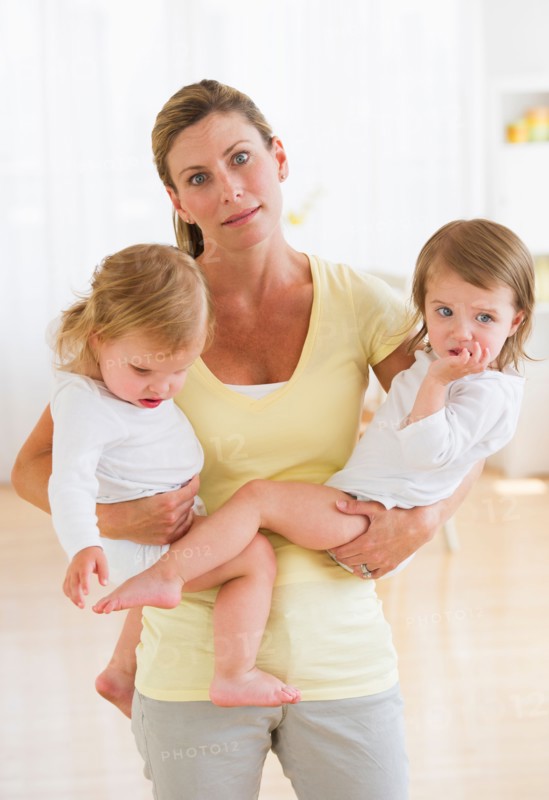 Mother holding daughters (2-3) and making facial expression.