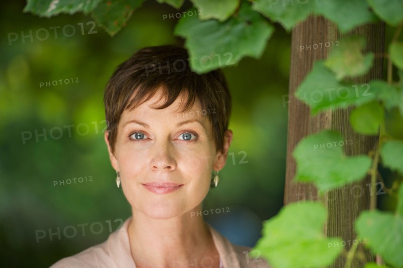 Portrait of mature woman standing next to ivy.