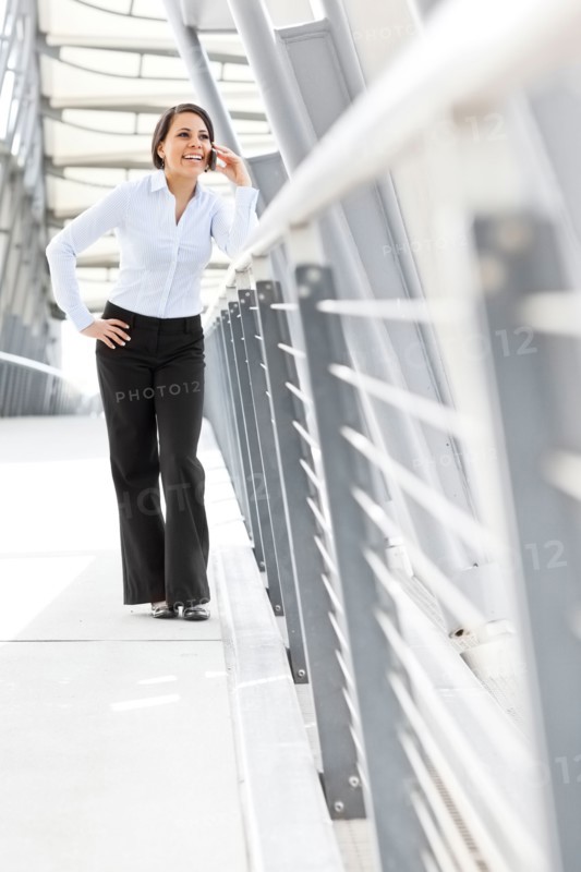 Young businesswoman on walkway, using cell phone. Photo: Take A Pix Media