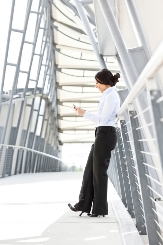 Young businesswoman on walkway, using cell phone. Photo: Take A Pix Media