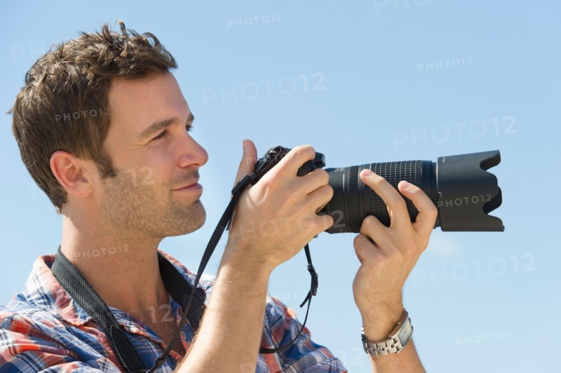 Man holding camera against blue sky.