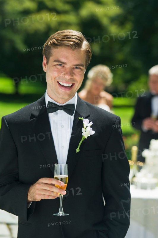 Portrait of groom holding champagne flute.