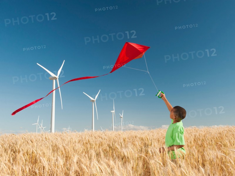 USA, Oregon, Wasco, Boy (8-9) playing with kite in wheat field, wind turbines in background. Photo: Erik Isakson