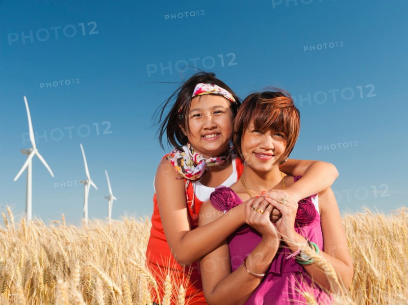 USA, Oregon, Wasco, Girl (10-11) and mother standing in wheat field in front of wind turbines.