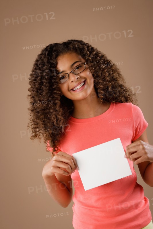 Studio portrait of girl (10-11) holding blank sheet of paper. Photo: Rob Lewine