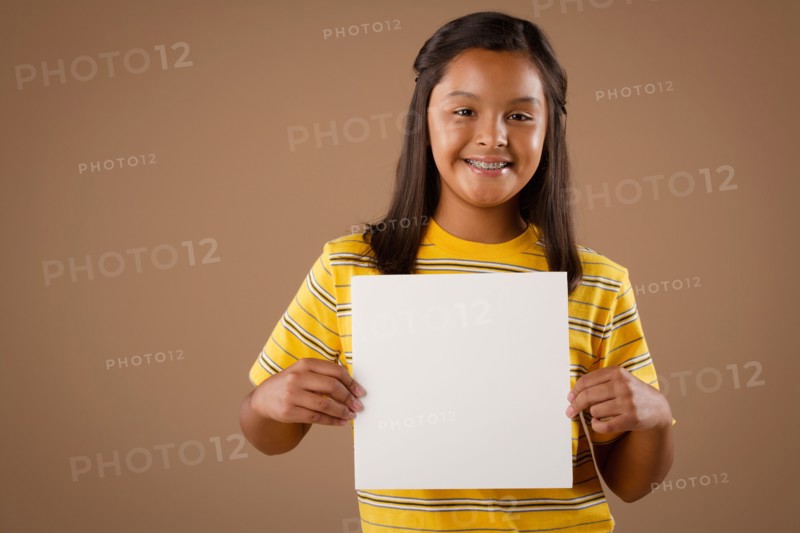 Studio portrait of girl (10-11) holding blank sheet of paper. Photo : Rob Lewine