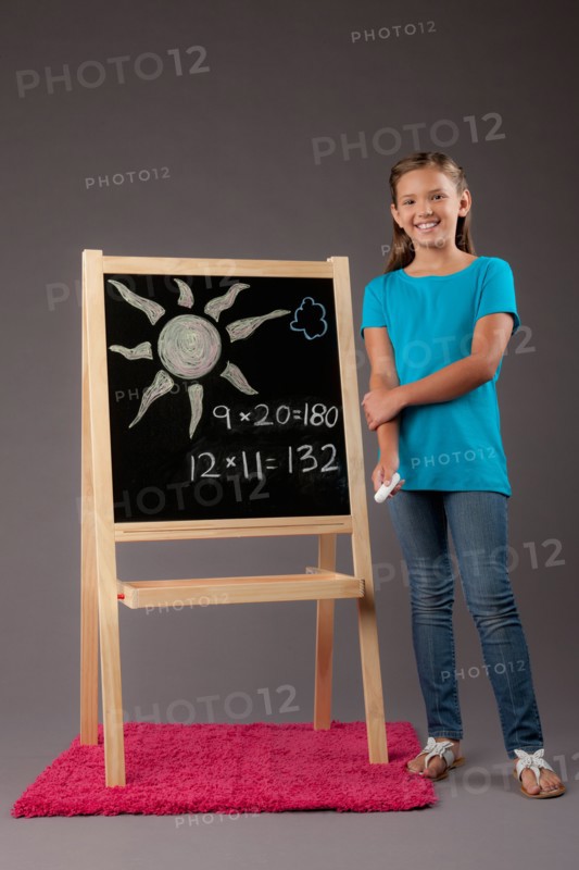 Studio portrait of girl (8-9) standing next to blackboard. Photo: Rob Lewine