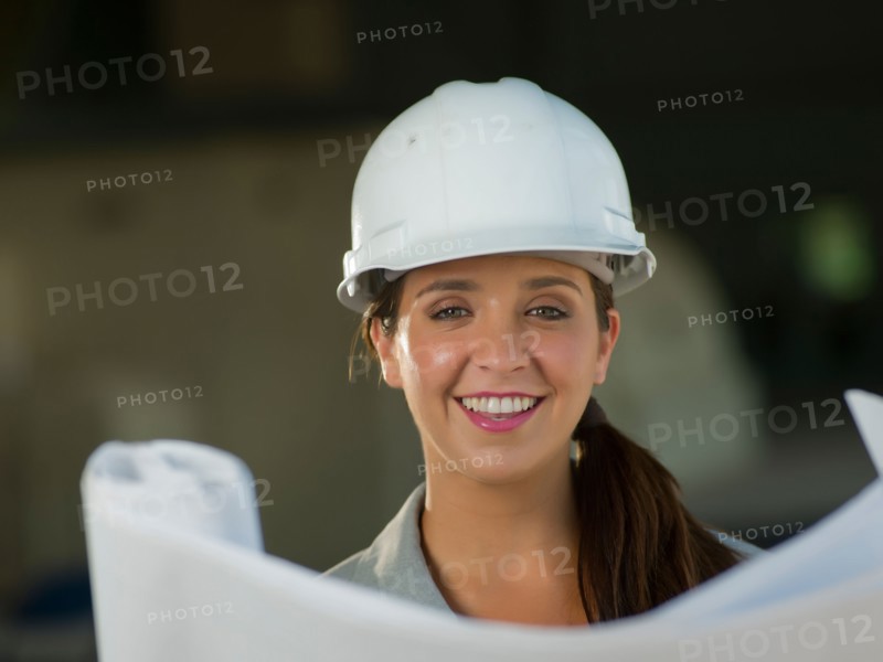 Portrait of woman wearing hardhat reading blueprint. Photo : db2stock