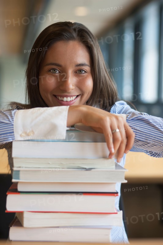 Portrait of female student leaning on stack of books. Photo : Jan Scherders