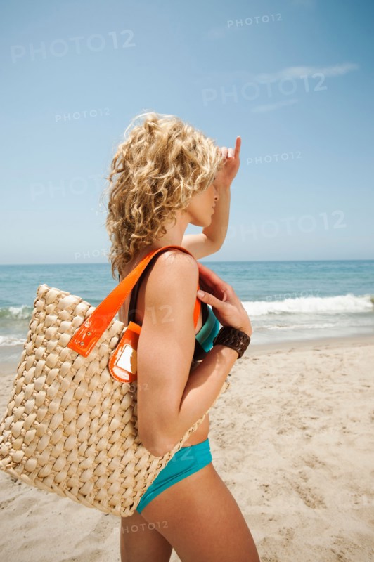 Young attractive woman carrying straw bag on sandy beach.