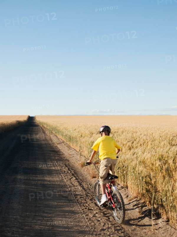 Boy (8-9) cycling along dirt road.