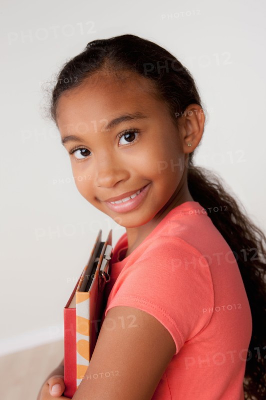 Studio portrait of girl (8-9) holding books. Photo : Rob Lewine
